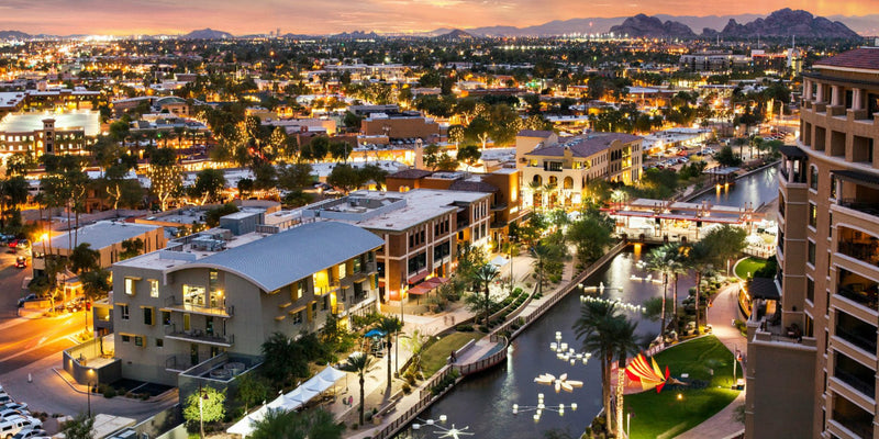 Aerial view of a cityscape with illuminated buildings and a canal at dusk.