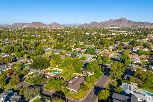 Aerial view of a suburban area with houses, trees, and mountains in the background.
